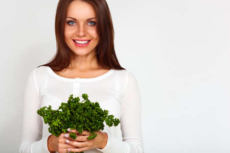 Young beautiful girl holding two bunches of parsley near the faceの写真素材