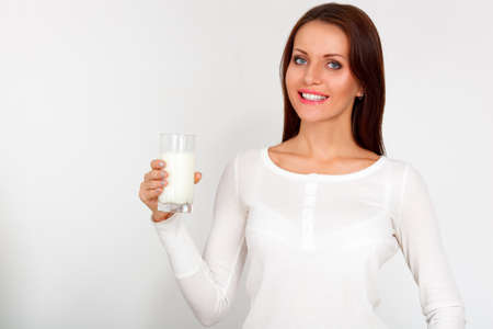 Young brunette woman drinking a glass of milk against a white backgroundの写真素材