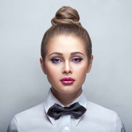 young blondie woman in white shirt and black bow-tie over whiteの写真素材