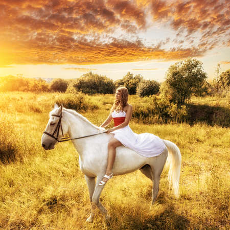 beautiful blonde woman on horse over sunsetの写真素材