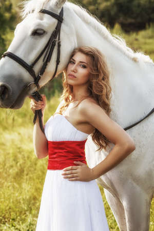 Beautiful women wearing white dress walking outdoors with white horse の写真素材