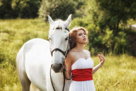 Beautiful women wearing white dress walking outdoors with white horse の写真素材