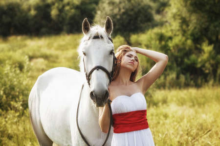 Beautiful women wearing white dress walking outdoors with white horse の写真素材