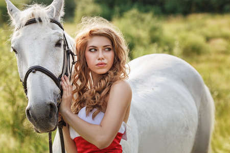 Beautiful women wearing white dress walking outdoors with white horse の写真素材