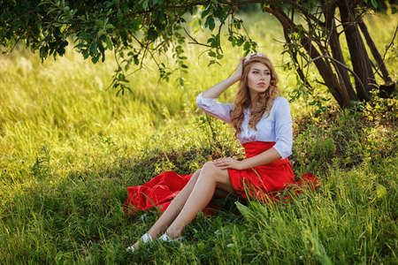 Romantic portrait of the woman in red skirt sitting under the treeの写真素材