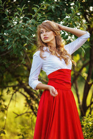 Romantic portrait of the woman in red skirt standing under the treeの写真素材