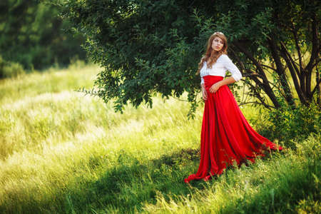Romantic portrait of the woman in red skirt standing under the treeの写真素材