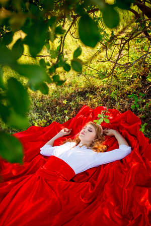 Romantic portrait of the woman in red skirt lying under the treeの写真素材