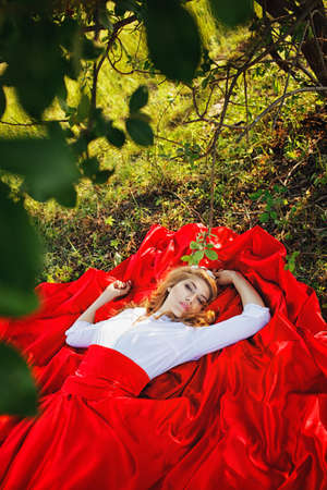 Romantic portrait of the woman in red skirt lying under the treeの写真素材