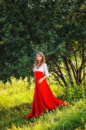Romantic portrait of the woman in red skirt standing under the treeの写真素材