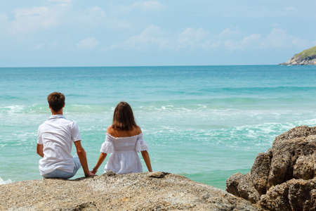 lovely young adult couple on the rocks above tropical sea, back viewの写真素材