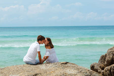 lovely young adult couple on the rocks above tropical sea, back viewの写真素材