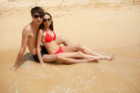 young adult happy couple in sunglasses sitting on the beachの写真素材