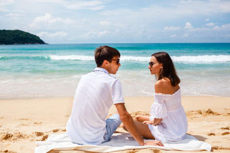 happy young adult couple sitting on a tropical beachの写真素材