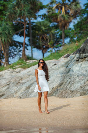happy brunette woman in white sun dress walking along the beachの写真素材