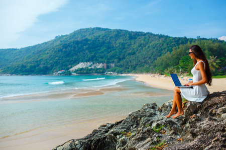 brunette woman sitting on the rock with laptop near  seaの写真素材