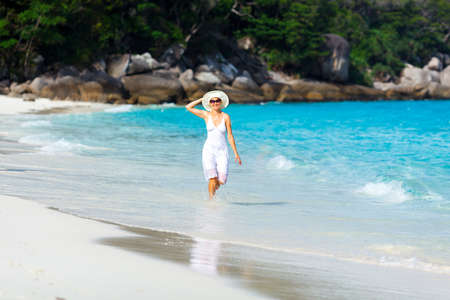 Young woman in a white dress walking on the tropical beautiful beachの写真素材