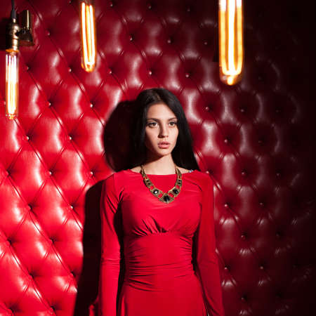 elegant sensual young brunette woman in red dress standing near wallの写真素材
