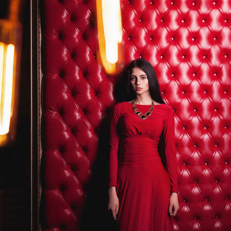 elegant sensual young brunette woman in red dress standing near wallの写真素材