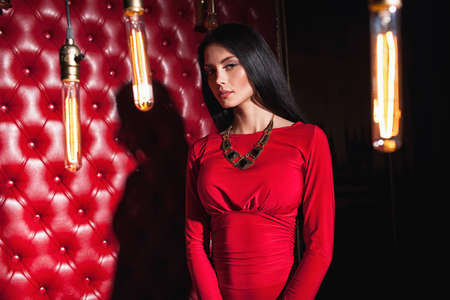 elegant sensual young brunette woman in red dress standing near wallの写真素材