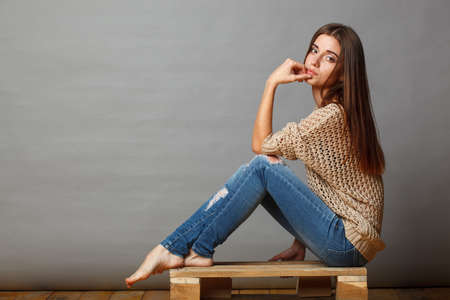 brunette woman sitting on wooden pallet over gray backgroundの写真素材