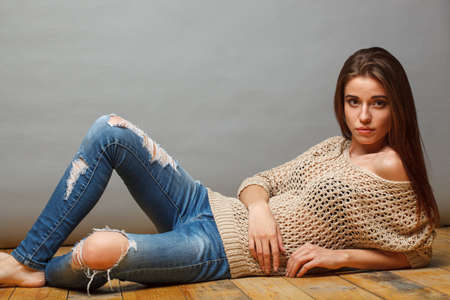 Brunette woman lying on wooden floor of studio over gray backgroundの写真素材