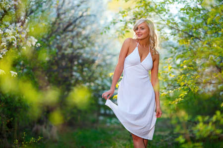 Beautiful happy young blonde woman enjoying smell in a flowering spring garden during sunsetの写真素材