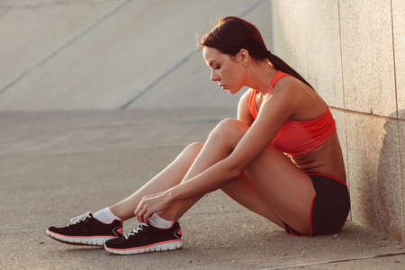brunette runner woman sitting on the ground and tie laces, sunset time, evening workoutの写真素材