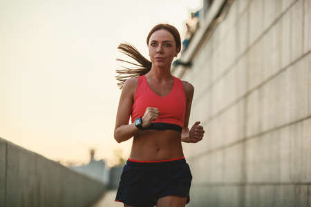 Girl runs along the concrete wall at sunset, wearing heart rate monitorの写真素材