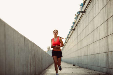 Girl runs along the concrete wall at sunset, wearing heart rate monitorの写真素材