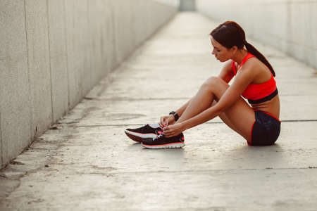 brunette runner woman sitting on the ground and tie laces, sunset time, evening workoutの写真素材