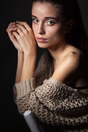 beautiful fashion model wearing hanging beige blouse sitting on chair over darkの写真素材