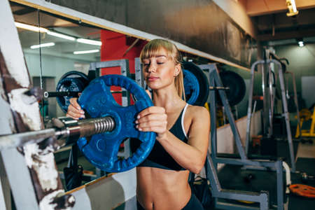 athletic young sexy girl sets weight on barbell in the gymの写真素材