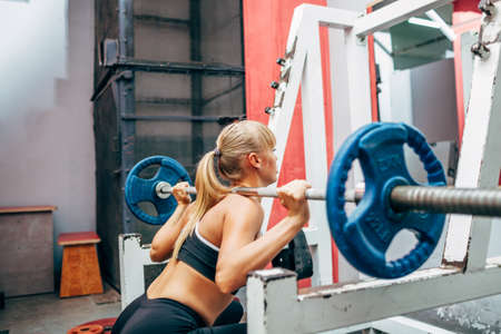 blonde strong fitness woman doing barbell squats in a gym