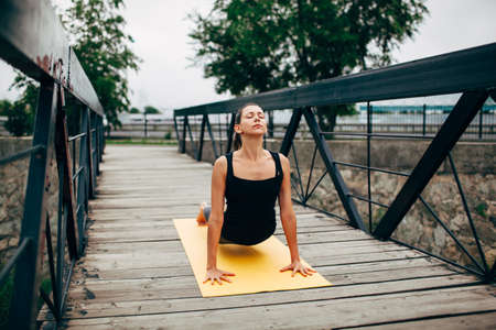 young slim woman doing yoga in the park on the wooden bridge, lying on floor