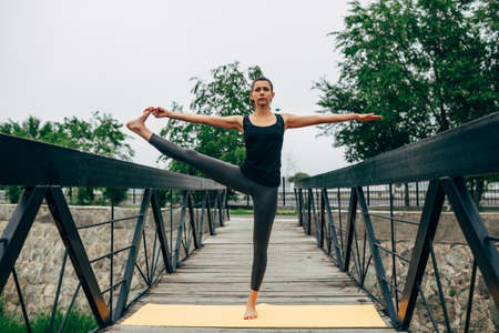 young slim woman doing yoga in the park on the wooden bridgeの写真素材