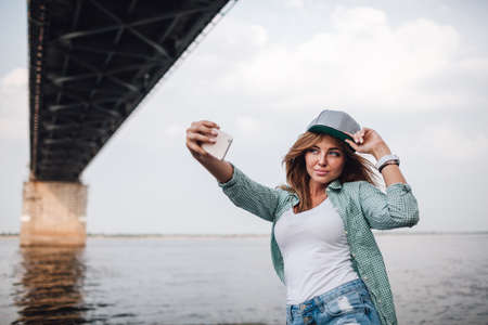 beautiful young adult woman taking picture of herself, selfie. She hold cap on her headの写真素材