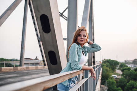 young adult beautiful woman standing on bridge , holding her hairs with handsの写真素材
