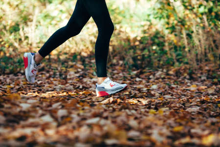 athlete woman runs for fall foliage, shoes closeup, motion blur effectの写真素材