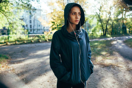 sporty woman wearing hood jacket and listening music outdoors in the park