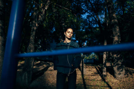 runner woman wearing gray jacket standing on sport square, film toned image, sunlight on her face