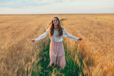 happy beautiful brunette smiling girl in wheat field at sunset, running among fieldの写真素材