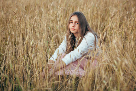 Young beautiful woman wearing white  and pink dress sitting in wheat fieldの写真素材