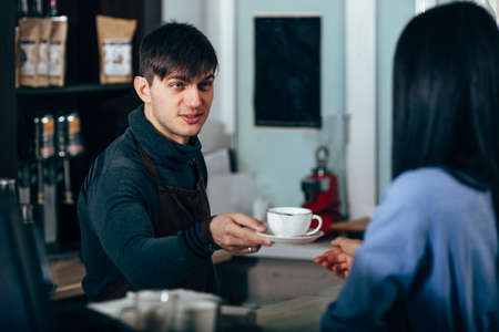 barista with beard hands takeaway coffee to brunette woman customer