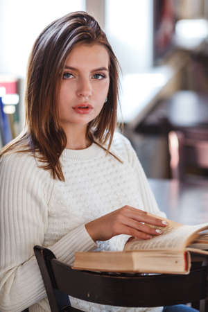 blonde woman reading book at cafe near window, looking at camera, vertical frameの写真素材
