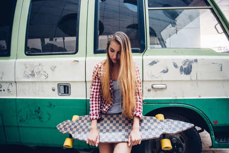 seriously young beautiful blonde woman with longboard standing near green bus and looking downの写真素材