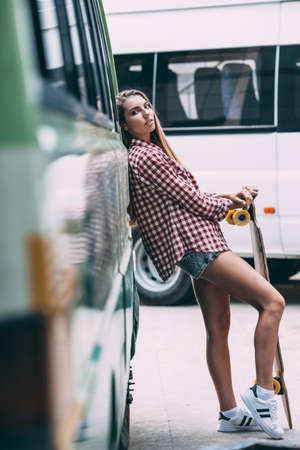 seriously young beautiful blonde woman with longboard standing near busの写真素材