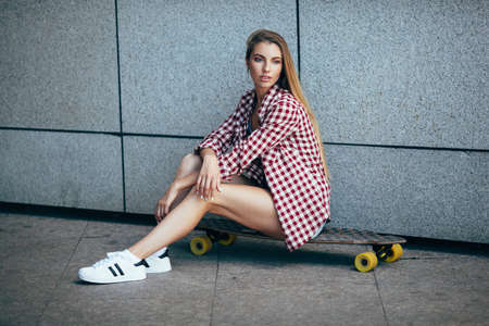 blond female in red plaid shirt posing with longboard near granite wallの写真素材