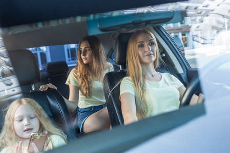 blonde beautiful woman with a smile driving a car. Her cute daughters sitting on rearの写真素材