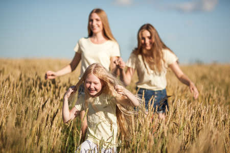 happy mother and her daugthers run on wheat fieldの写真素材